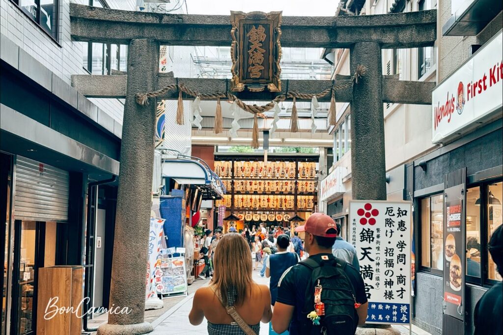 錦天滿宮入口處的灰色鳥居,前面站著一對外國人旅客