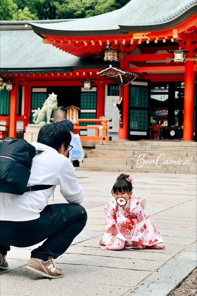 身穿粉色和服的日本小女孩在神戶生田神社前拍照，身旁有爸爸當作攝影師