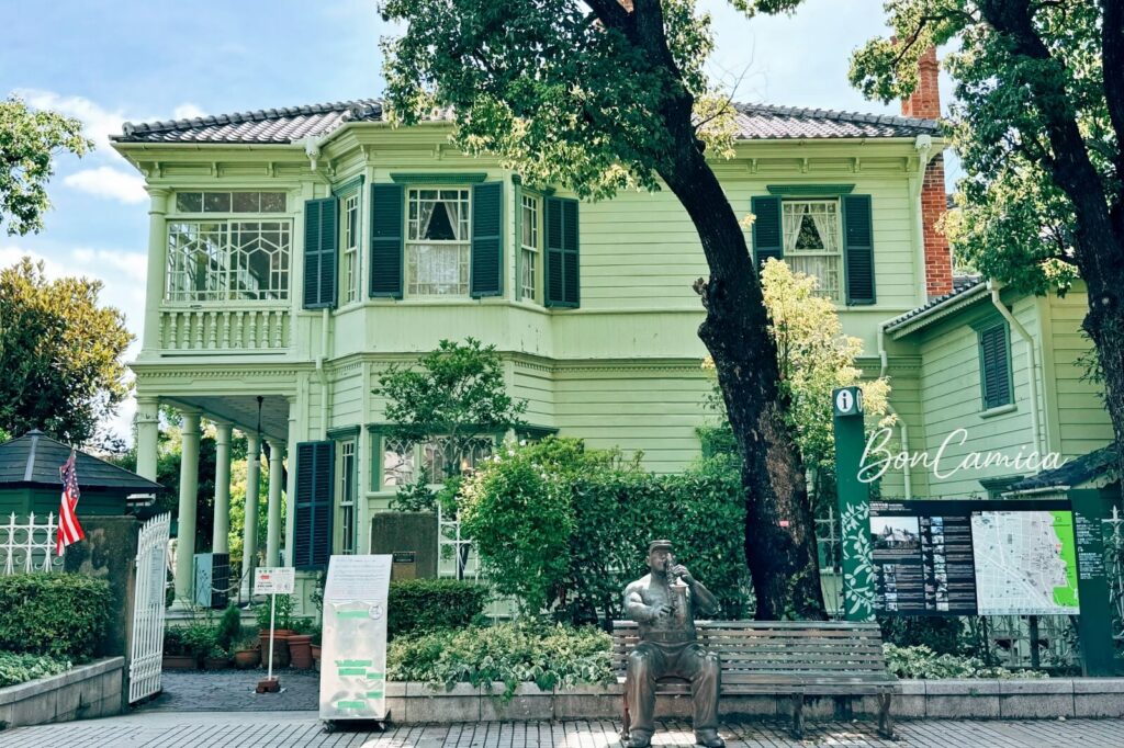 藍天白雲之下的萌黃之館，復古草綠色的歐式建築，前方有吹小號的大叔青銅雕像